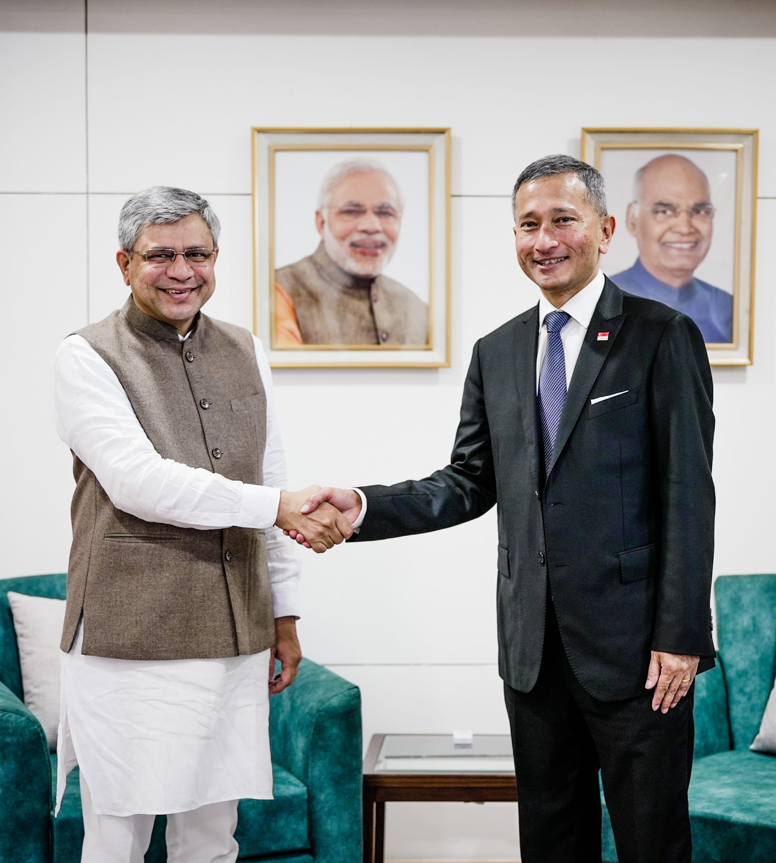 Man in suit holding hands of woman in wheelchair at event. Tables set in background.